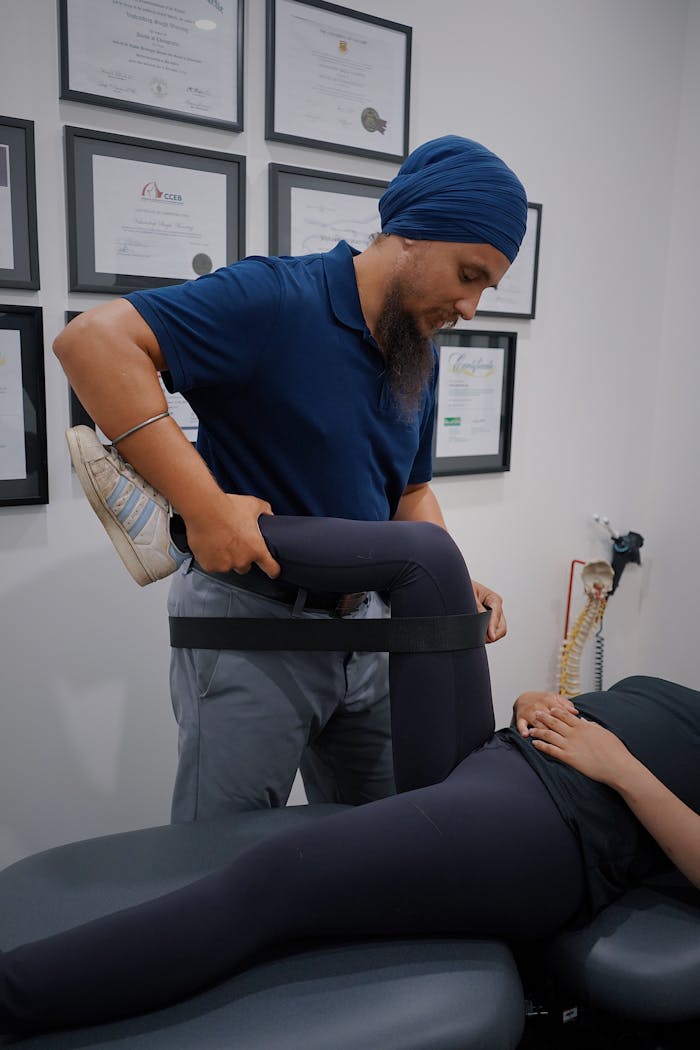Male physiotherapist with turban helping female patient with leg rehabilitation exercise in a modern clinic setting.